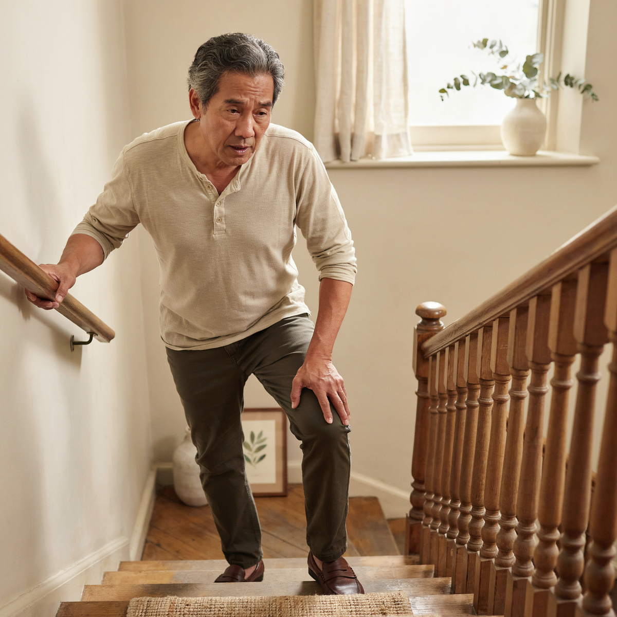 Hombre apoyándose en el pasamanos a mitad de una escalera por dolor de rodilla